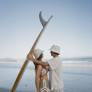 Couple wearing Will & Bear removable string bucket hats on the beach, perfect for sun protection and surfside adventures.